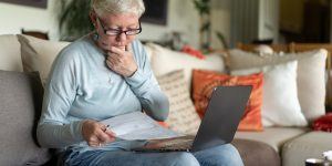 With her hand on her chin, a mature lady puzzles at her monthly finances